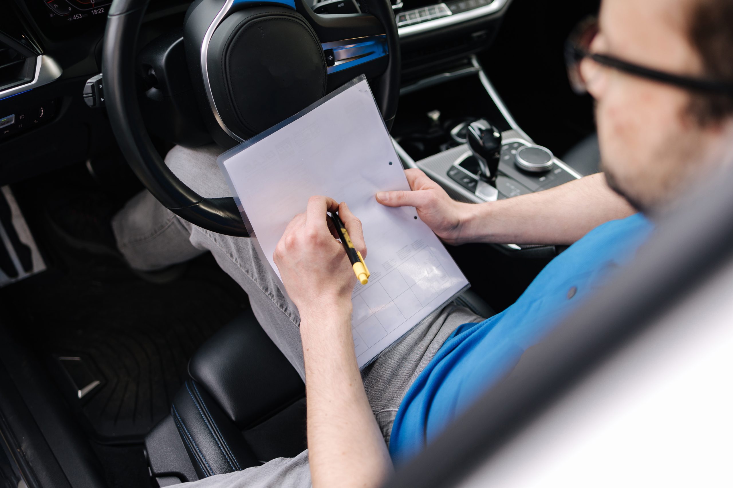 Side View On Male Mechanic Fill Document During Car Inspection. Man Sits Inside Car And Looks At The Paper